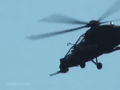 A Military Helicopter Is Flying In A Blue Sky . GIF