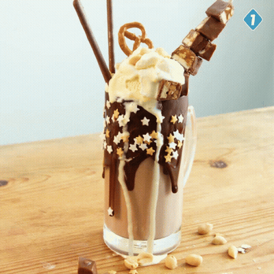 A Milkshake With Ice Cream Pretzels And Chocolate On A Table GIF