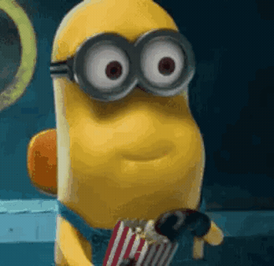 A Minion Wearing Goggles Is Holding A Bag Of Popcorn And A Chocolate Bar . GIF