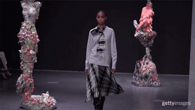 A Model Walks Down The Runway At A Fashion Show Surrounded By Sculptures GIF