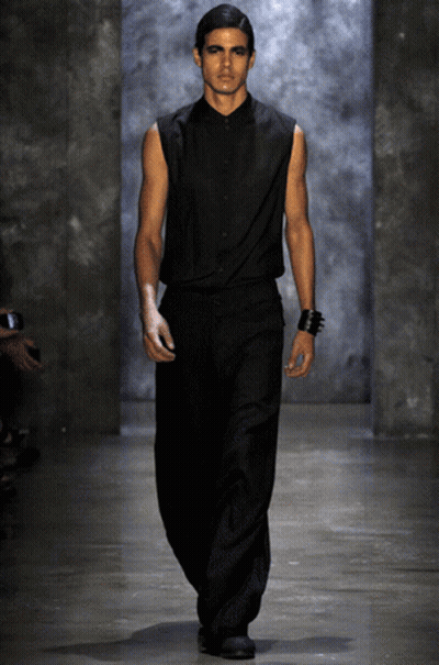 A Model Walks Down The Runway At A Fashion Show Wearing A Black Shirt And Black Pants GIF