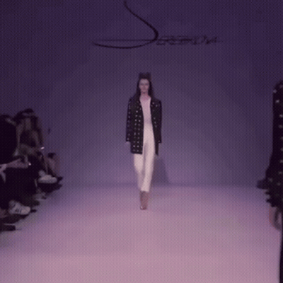 A Model Walks Down The Runway At A Fashion Show With A Purple Background GIF
