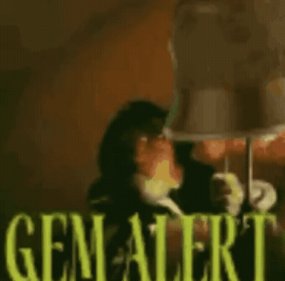 A Monkey Is Sitting In Front Of A Lamp With The Words `` Gem Alert '' Written In Yellow Letters . GIF