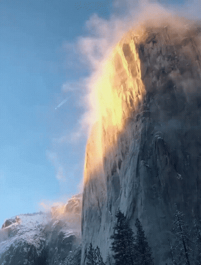 A Mountain Covered In Snow And Trees With The Sun Shining On It GIF