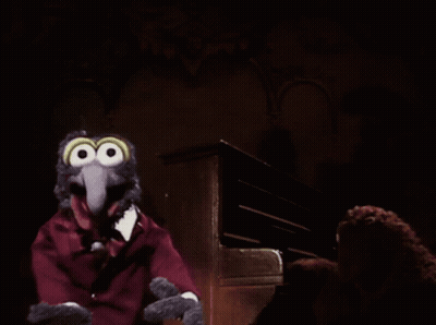 A Muppet With Big Eyes And A Red Suit Is Sitting In Front Of A Piano GIF