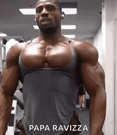 A Muscular Man In A Grey Tank Top Is Standing In A Gym With Papa Ravizza Written On The Bottom Of His Chest . GIF