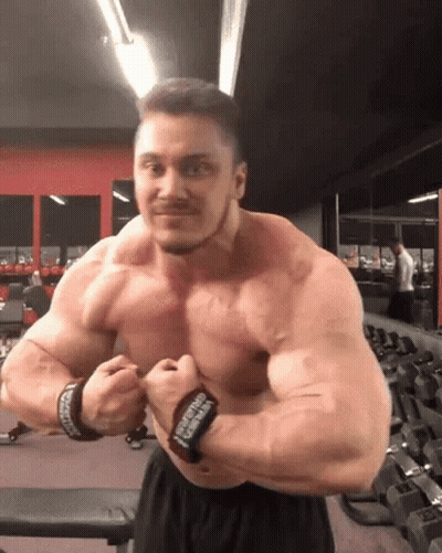 A Muscular Man Is Posing For A Picture In A Gym . GIF