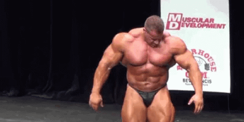 A Muscular Man Is Standing On A Stage In Front Of A Screen . GIF