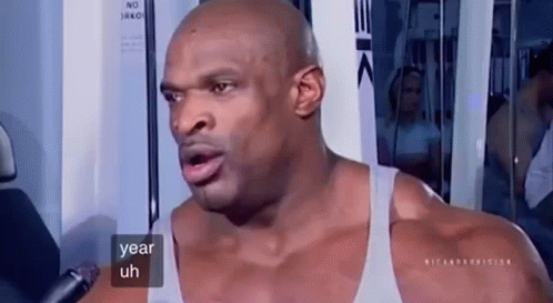 A Muscular Man Is Talking Into A Microphone While Sitting On A Machine In A Gym . GIF