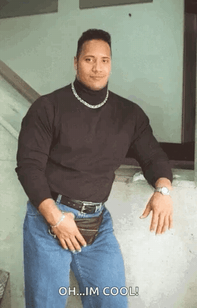 A Muscular Man Wearing A Black Turtleneck And Jeans Is Standing In Front Of A Wall . GIF