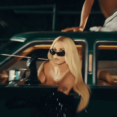 A Naked Blonde Woman Wearing Sunglasses Is Sitting In A Car GIF