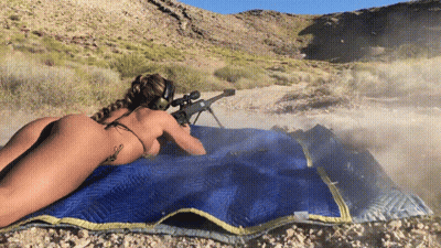 A Naked Woman In A Bikini Is Laying On A Blue Blanket Holding A Rifle GIF