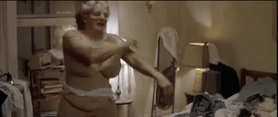A Naked Woman Is Standing In A Messy Room With A Mirror . GIF