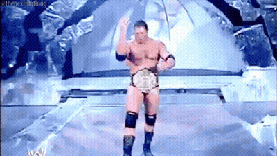 A Naked Wrestler Is Standing On A Stage With A Wrestling Championship Belt . GIF