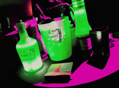 A Neon Green Bottle Of Hennessy Sits On A Pink Table GIF