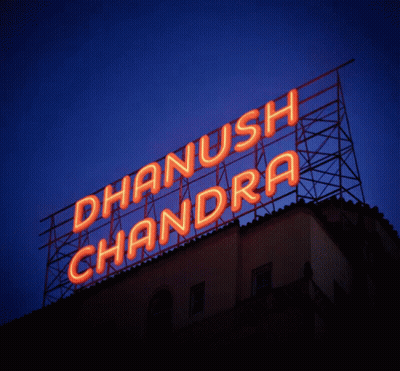 A Neon Sign For Dhanush Chandra Is Lit Up In Orange GIF