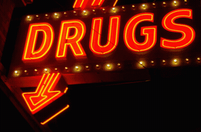 A Neon Sign That Says " Drugs " Is Lit Up At Night GIF
