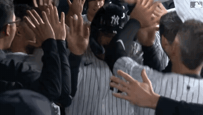 A New York Yankees Baseball Player Is Surrounded By His Teammates Giving Him A High Five GIF