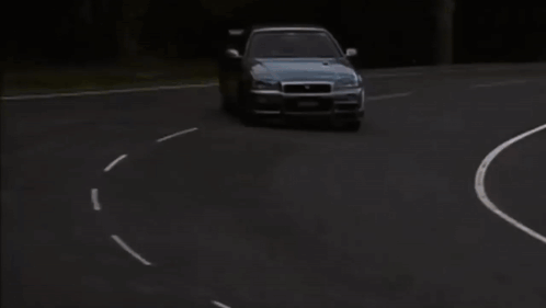 A Nissan Car Is Driving Down A Road With A Grassy Hill In The Background GIF