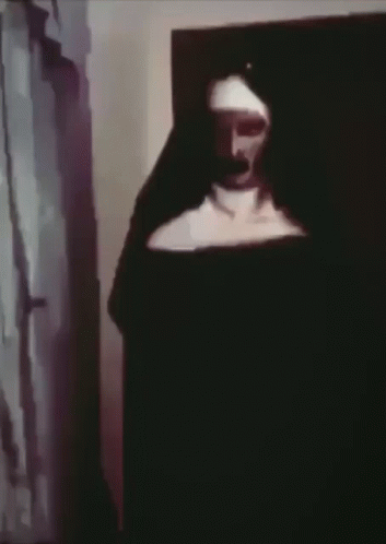 A Nun Is Standing In A Dark Room With A Black Background . GIF