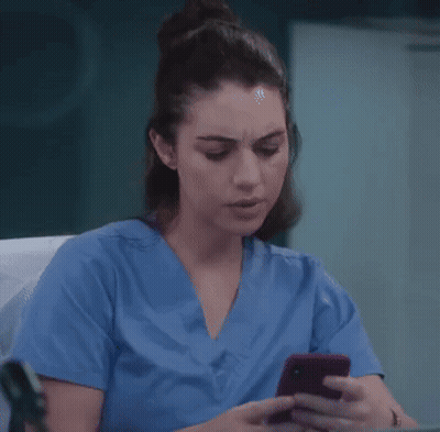 A Nurse In A Blue Scrub Top Is Looking At Her Cell Phone . GIF