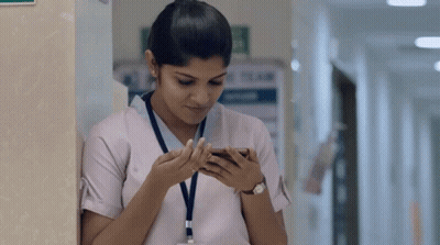 A Nurse Is Leaning Against A Wall And Looking At Her Phone GIF