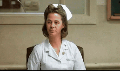 A Nurse Is Sitting In A Chair In A Hospital Room Wearing A White Nurse 'S Cap . GIF