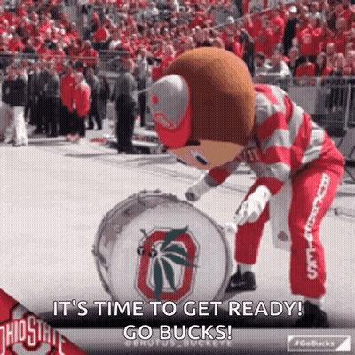 A Ohio State Mascot Is Playing A Drum In Front Of A Crowd Of People . GIF