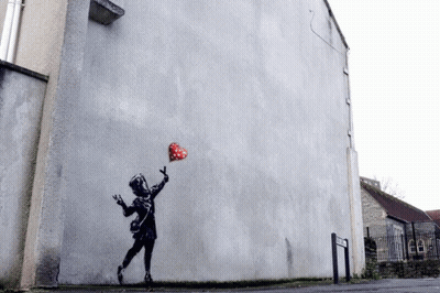 A Painting Of A Girl Holding A Heart Shaped Balloon On The Side Of A Building GIF