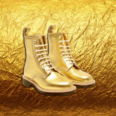 A Pair Of Gold Boots With White Laces Are Against A Gold Background GIF