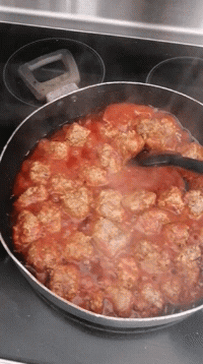 A Pan Filled With Meatballs And Sauce Is Cooking On A Stove GIF