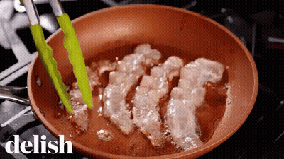 A Pan Of Bacon Is Being Cooked On A Stove With The Word Delish In The Upper Right Corner GIF
