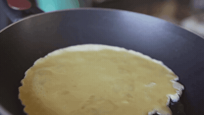 A Pancake Is Being Cooked In A Frying Pan With Oil . GIF