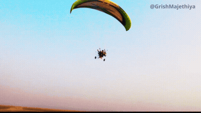 A Paraglider Is Flying Through A Blue Sky With The Hashtag @Grishmajethiya On The Bottom GIF