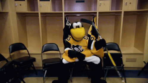 A Penguin Mascot In A Pittsburgh Penguins Jersey Sits In A Locker Room Holding A Hockey Stick GIF