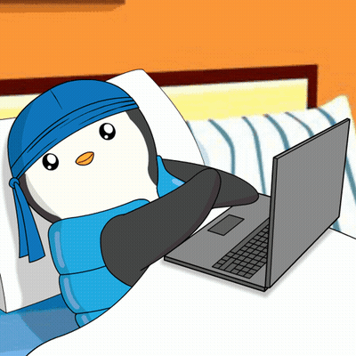 A Penguin Wearing A Blue Bandana Is Laying On A Bed Next To A Laptop GIF