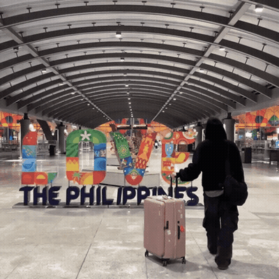 A Person Carrying A Suitcase Walking In Front Of A Sign That Says The Philippines GIF