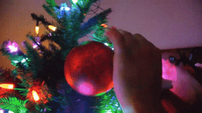 A Person Decorates A Christmas Tree With A Red Ball GIF