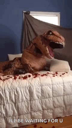 A Person Dressed As A T-Rex Is Sitting On A Bed . GIF
