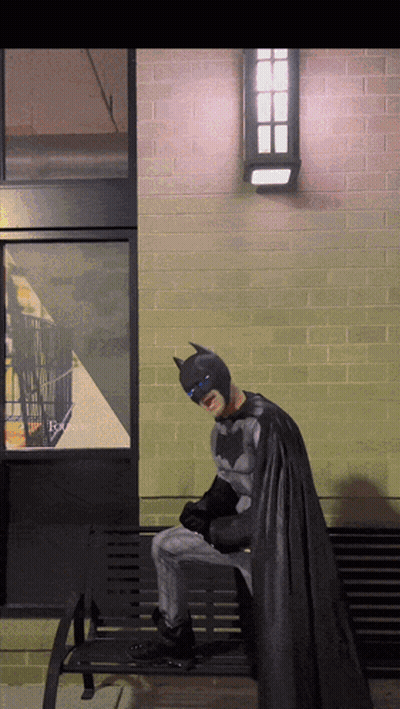 A Person Dressed As Batman Sits On A Bench GIF