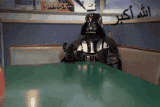 A Person Dressed As Darth Vader Sits At A Table In A Diner GIF