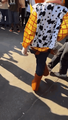 A Person Dressed As Woody From Toy Story Walking Down A Sidewalk GIF