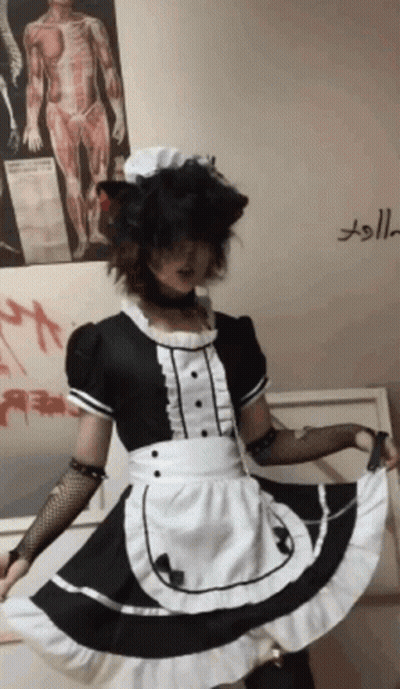 A Person Dressed In A Maid Costume Is Standing In Front Of A Wall With A Poster Of A Man 'S Anatomy GIF