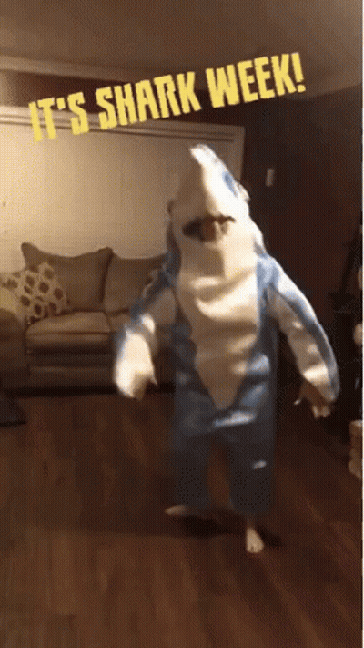A Person Dressed In A Shark Costume With The Words It 'S Shark Week Behind Them GIF
