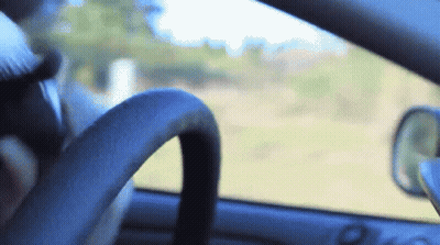 A Person Driving A Car With A Steering Wheel In The Foreground And A Rear View Mirror In The Background GIF