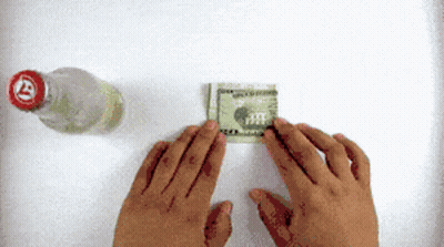 A Person Folding A Dollar Bill Next To A Bottle With A Red Cap GIF