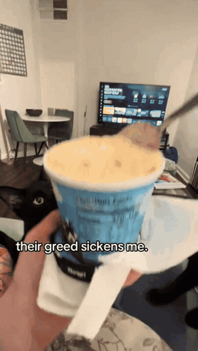 a person holding a cup of ice cream that says " their greed sickens me " on it