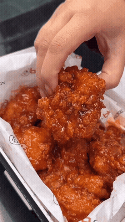 A Person Holding A Piece Of Fried Chicken Over A Box Of Chicken GIF