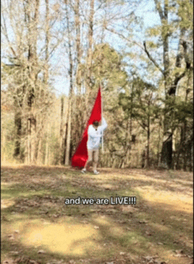 A Person Holding A Red Flag With The Words And We Are Live Written On The Bottom GIF