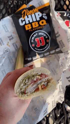 A Person Holding A Sandwich Next To A Bag Of Jimmy John 'S Bbq Chips GIF